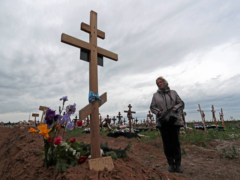 Mulher é retratada ao lado do túmulo de filho em um cemitério em Staryi Krym nos arredores de Mariupol, Ucrânia