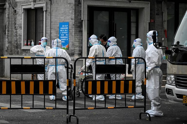 Imagem mostra seis trabalhadores com roupas brancas de proteção e máscaras em ação contra o coronavírus em uma rua de Pequim, na China  