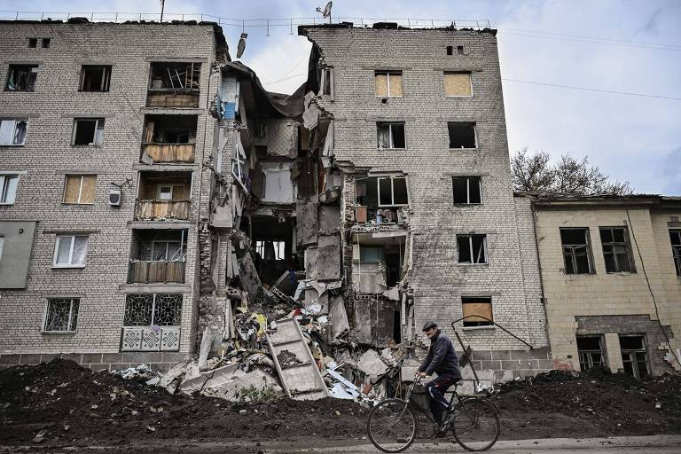 Homem anda de bicicleta em frente a prédio destruído na cidade de Bakhmut, na região do Donbas, na Ucrânia 