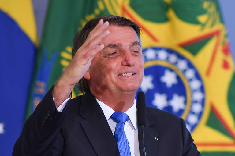 O presidente Jair Bolsonaro acena com a mão direita em evento no Palácio do Planalto, em Brasília; ele usa terno preto, gravata azul e camisa branca