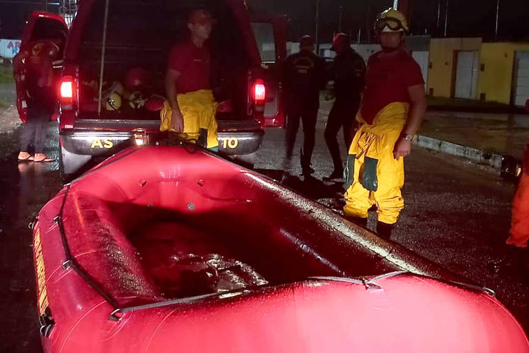 foto noturna de três bombeiros com bote e ambulância na rua