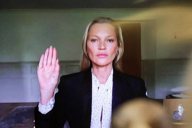 Kate Moss, de camisa branca e blazer preto, com a mão direita levantada, no momento em que faz o juramento de dizer a verdade, em imagem de vídeo
