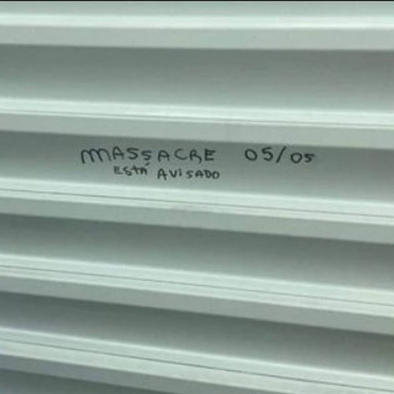 Pichação de caneta preta em porta branca "Massacre 05/05 está avisado"