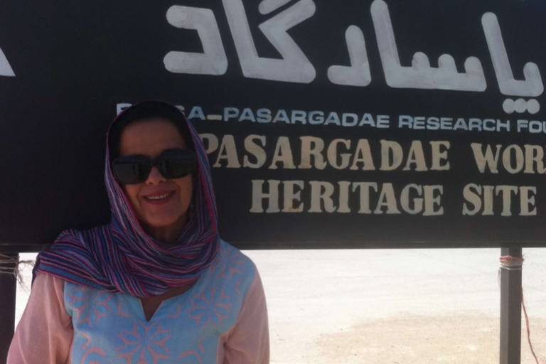 Mulher com o cabelo coberto por um véu posa diante de uma placa com dizeres em persa