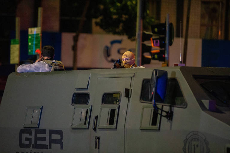 Policiais seguram armas em cima de veículo; um deles está mascarado