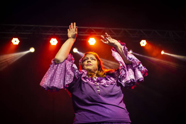 Mulher ergue os braços em uma dança sob as luzes do palco