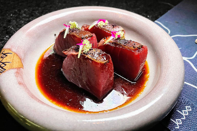 A foto mostra quatro fatias de atum sobre um molho escuro em um prato de cerâmica branco