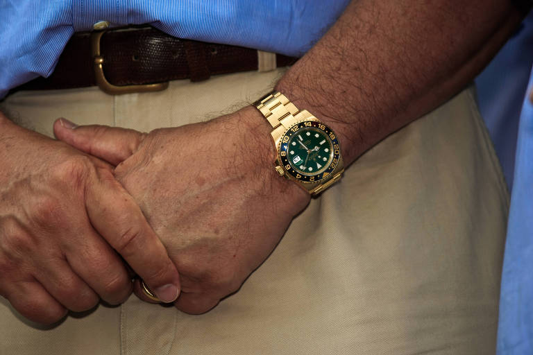 Imagem mostra mão de homem branco, com um relógio dourado no pulso