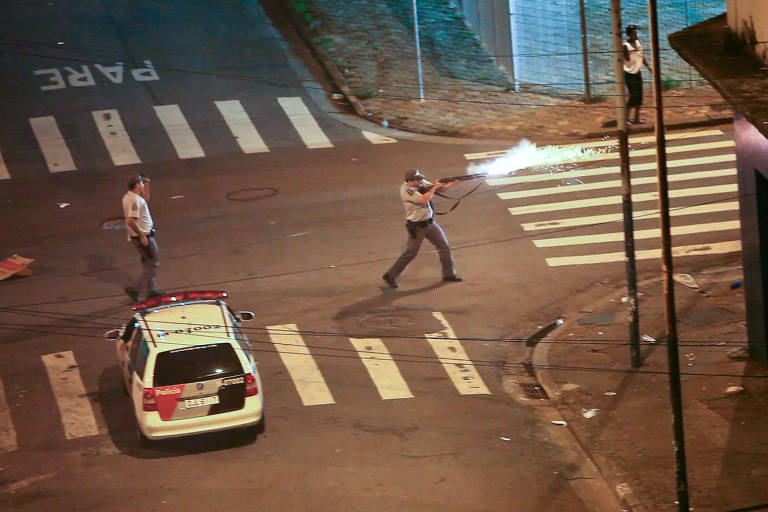 Policial é visto de longe, atirando em uma rua; os alvos não aparecem