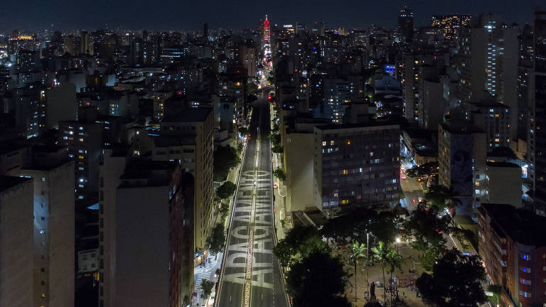 Imagem aérea mostra o Elevado Presidente João Goulart, o popular Minhocão, fechado a noite para lazer em meio a prédios e árvore, escrito no asfalto 'apagamento' como forma de protesto a falta de iluminação no local 