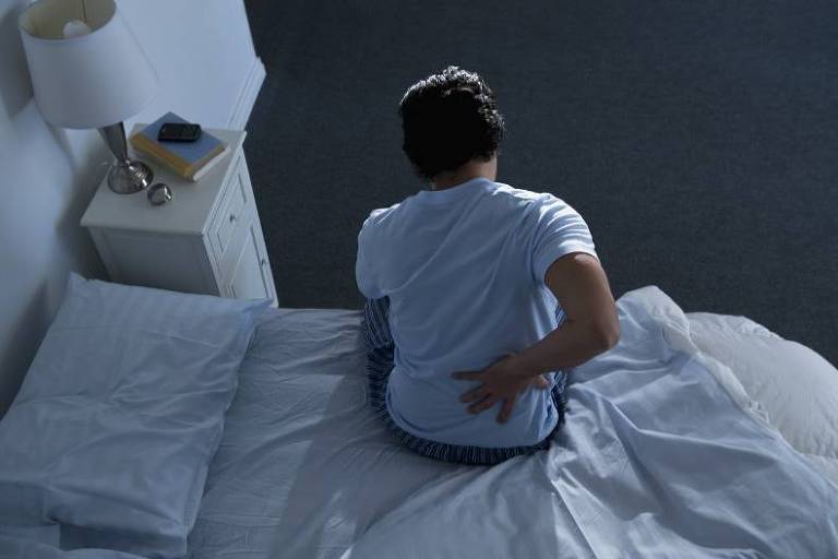 Homem sentado na cama com uma mão nas costas