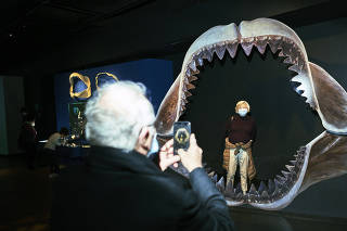 A visitor poses for a photo while standing inside replica jaws of the megalodon on display at the American Museum of Natural History in Manhattan on Dec. 10, 2021. (An Rong Xu/The New York Times)