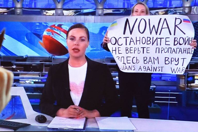 A âncora de notícias Yekaterina Andreyeva apresenta o jornal, e Marina Ovsyannikova, que usava um terno formal escuro, aparece atrás, segurando um pôster escrito à mão dizendo "sem guerra" em inglês