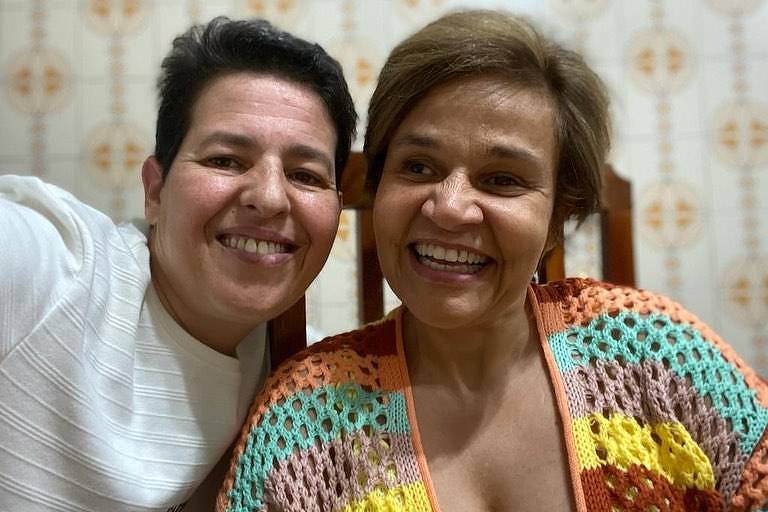 Duas mulheres posando para selfie. A da direita veste uma blusa de crochê colorida, já a da esquerda veste uma camiseta branca