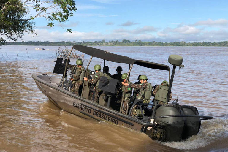 Barco militar com cerca de dez militares com roupa camuflada, em rio de águas barrentas