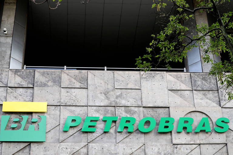 Parede recoberta de pedras, com Petrobras escrita em letras verdes e símbolo amarelo e verde, quadrado,com as letras BR