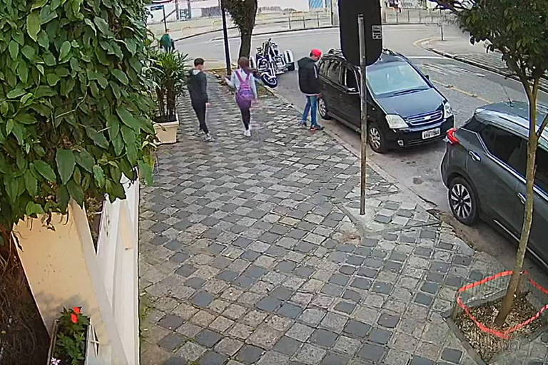 Câmera de segurança mostra calçada com carro estacionado, dupla de jovens passando e homem entrando no carro