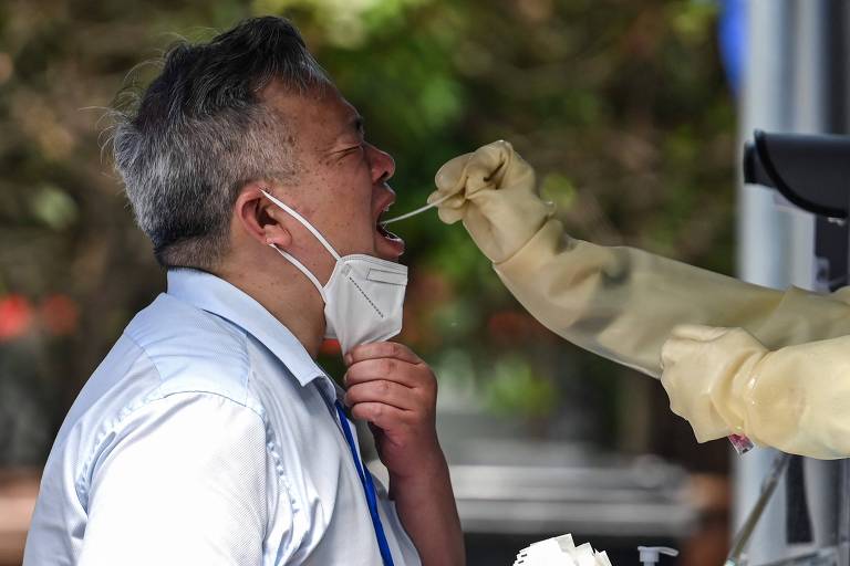 Imagem mostra homem com a máscara abaixada e com a boca aberta. Um profissional de saúde insere um cotonete dentro da boca do homem.