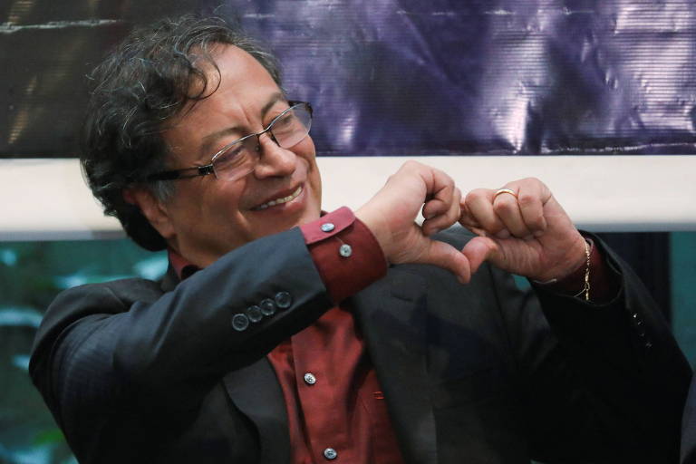 Sorrindo, Gustavo Petro, candidato da esquerda na eleição para a Presidência da Colômbia, faz com as mãos o formato de um coração em encontro com pessoas deficientes em Bogotá; ele usa óculos, sua camisa é vinho e o paletó é azul escuro