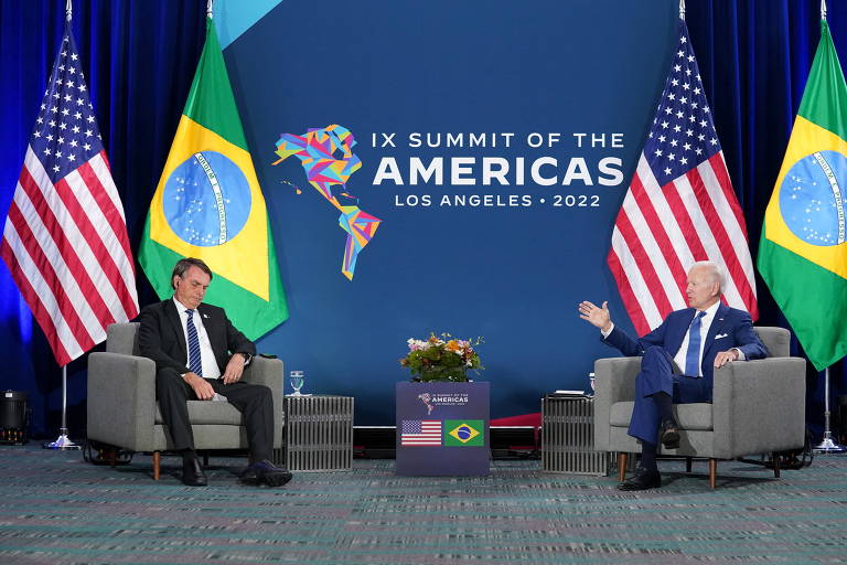 Em palco com duas poltronas afastadas estão sentados à esquerda Jair Bolsonaro e à direita Joe Biden. Ele fala gesticulando com a mão, enquanto Bolsonaro olha para baixo. Atrás de cada um deles, uma bandeira dos EUA e uma do Brasil