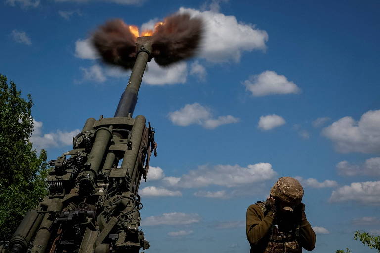 Soldado ucraniano tapa os ouvidos durante disparo de um obuseiro americano M777 na área de Donetsk