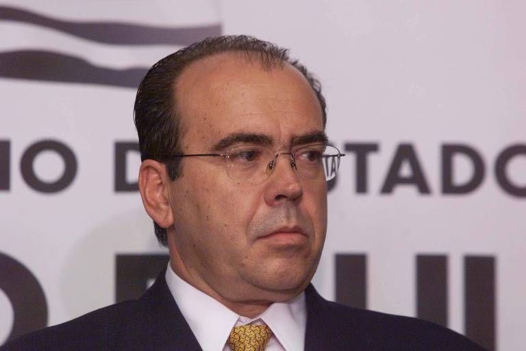 Imagem mostra Dario Rais Lopes, um homem branco, um pouco calvo, que usa óculos e terno. Ele está olhando para o lado direito.