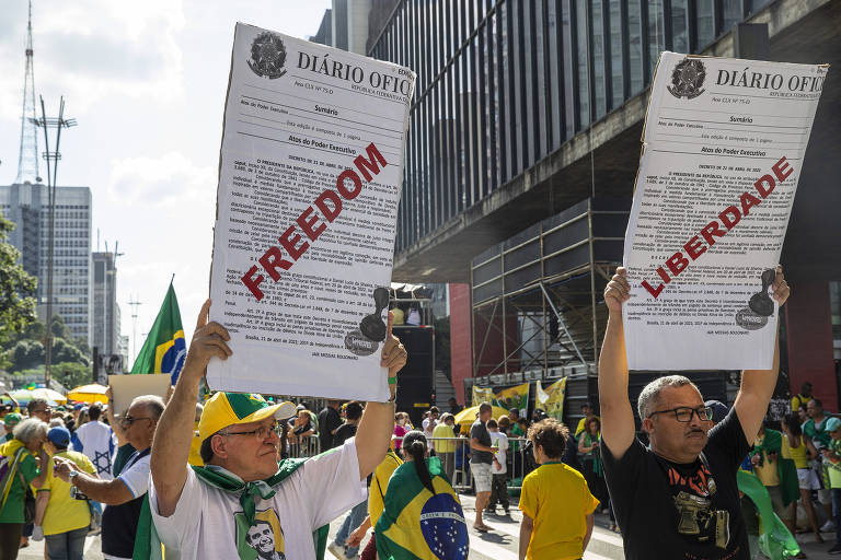 Manifestantes pró Bolsonaro seguram cartazes com emulação do diário oficial e as tarjas freedom e liberdade