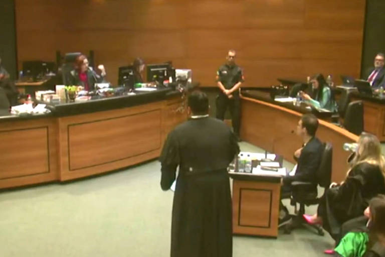 sala do tribunal do juri do Rio, com juiza, advogados de toga preta e réu sentado falando ao microfone em tribuna de madeira