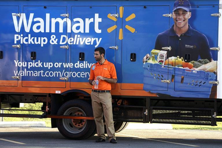 Imagem mostra homem, vestido com uniforme laranja do Walmart e calça cargo, encostado em um caminhão da varejista e com as mãos dentro de um saco de biscoitos. O caminhão é azul, laranja e tem a logo do Walmart, além da imagem de um homem segurando uma cesta de produtos.