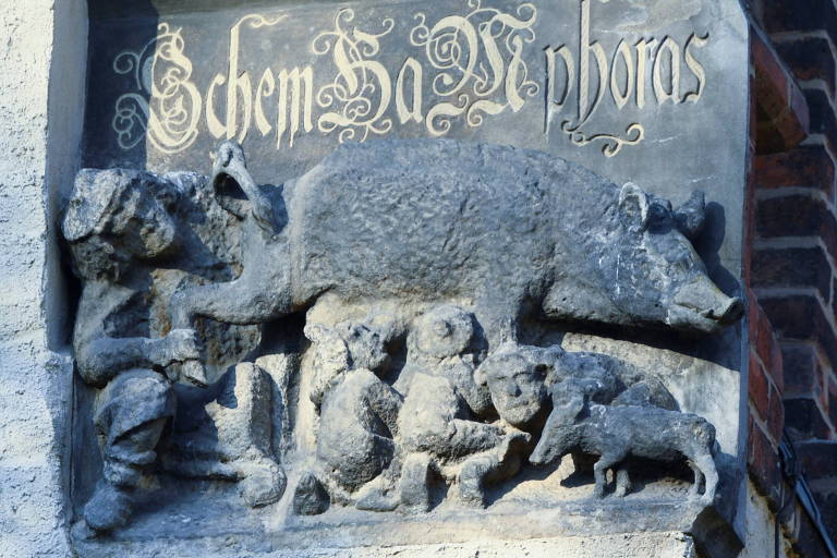 Escultura mostra um rabino olhando sob o rabo de uma porca, enquanto crianças amamentam nas tetas do animal