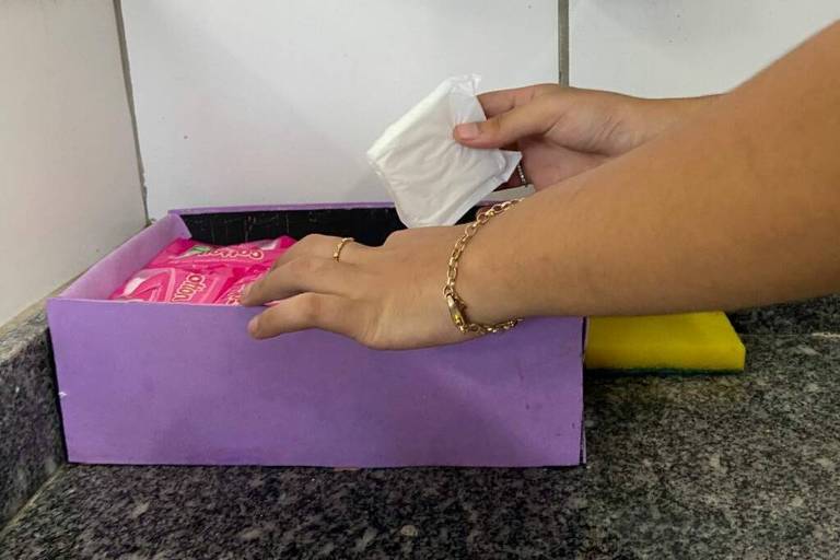 Mão de mulher pega  um absorvente em uma caixa roxa 