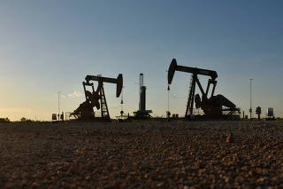 FILE PHOTO: Pump jacks operate in front of a drilling rig in an oil field in Midland