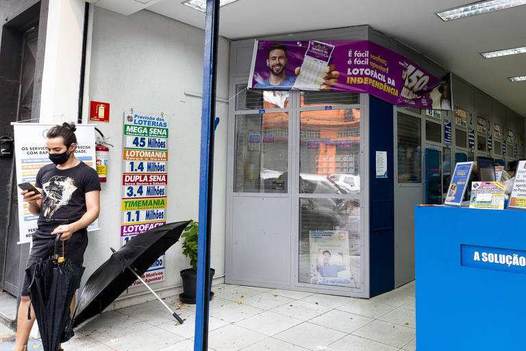 Imagem mostra pessoa mexendo no celular em frente a uma loteria.