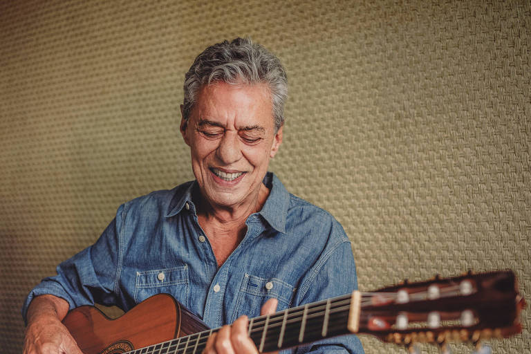 O artista Chico Buarque toca violão e sorri