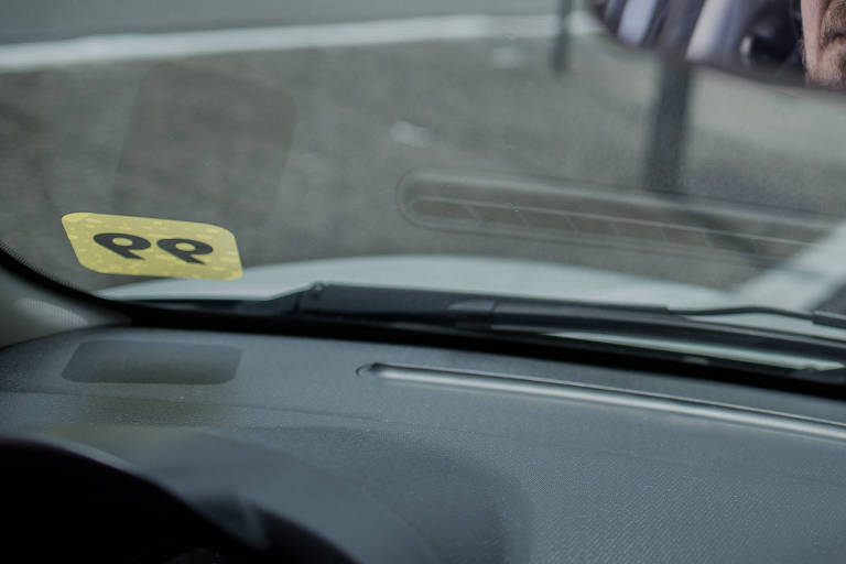 Homem de óculos escuros dirige carro com logotipo amarelo em que se lê 99