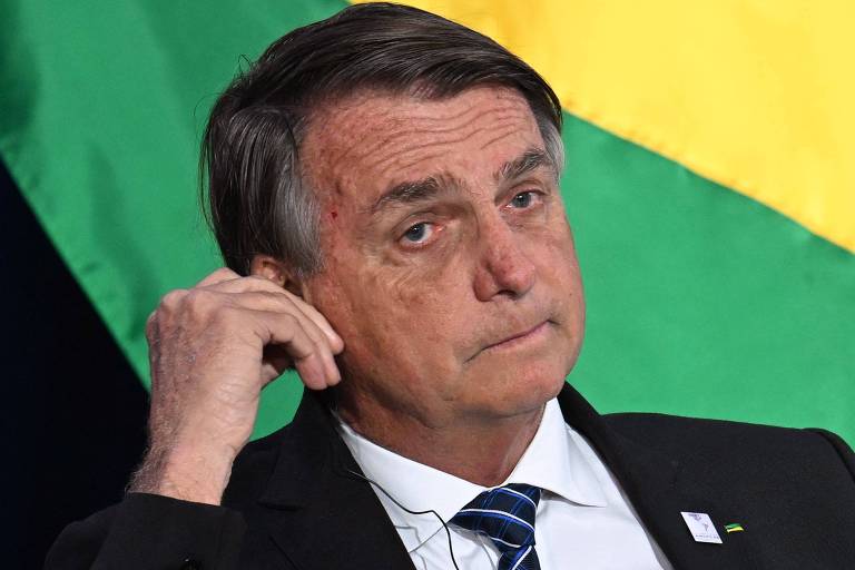 Bolsonaro ajusta fone de ouvido em frente a banceira do Brasil
