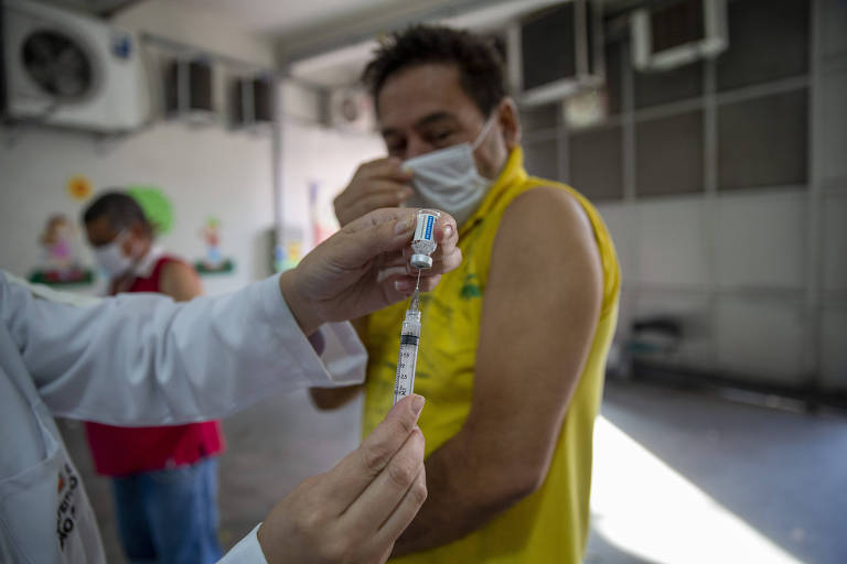 Agente de saúde prepara vacina para ser aplicada em homem
