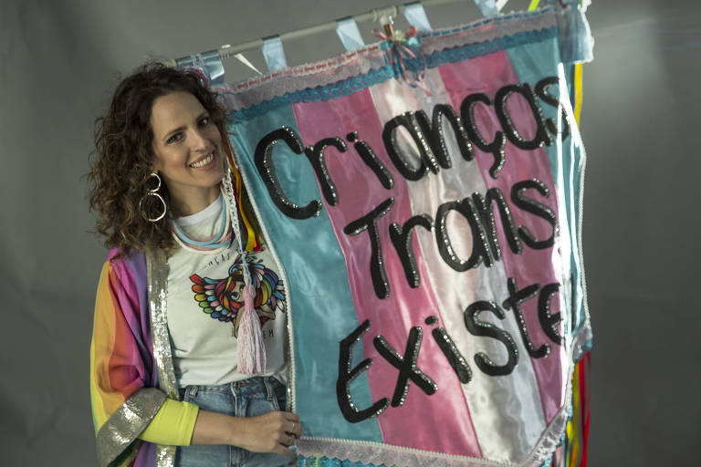 Thamirys Nunes segura bandeira rosa, branca e azul com os dizeres Crianças Trans Existem