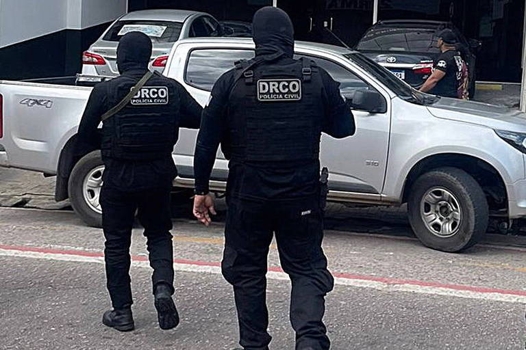 dois policiais de preto e gorro preto com iniciais nas costas DRCO Policia civil