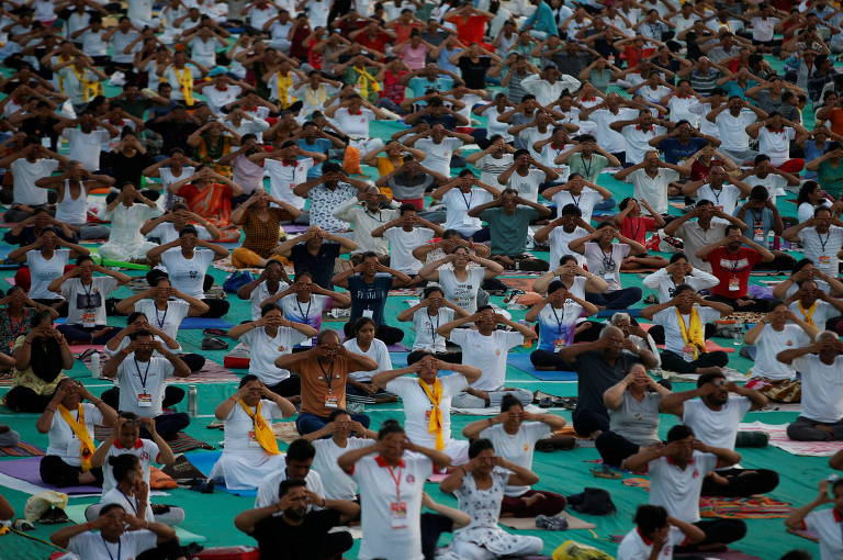 Uma multidão enfileirada sentada com pés cruzados num movimento de ioga