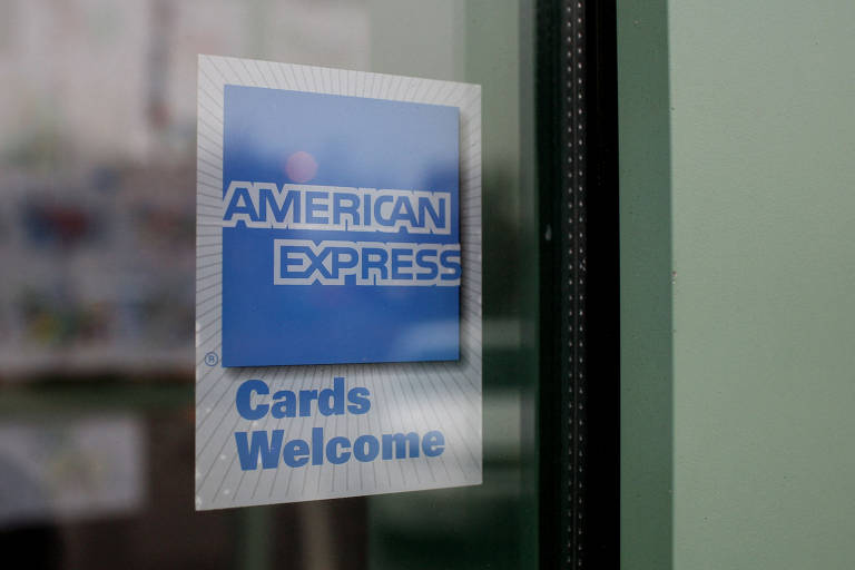 A logo da American Express na vitrine de uma loja. Abaixo está escrito "Cards Welcome", indicando que os cartões são aceitos no estabelecimento.