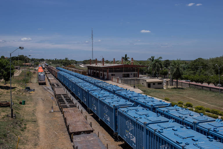 Imagem mostra vagões de carga parados sobre linha férrea em uma cidade rural