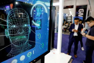 FILE PHOTO: Visitors check their phones behind the screen advertising facial recognition software during Global Mobile Internet Conference (GMIC) at the National Convention in Beijing