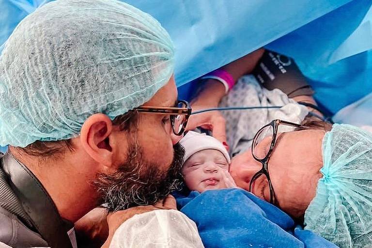 Em foto colorida, casal beija recém-nascido logo após o parto