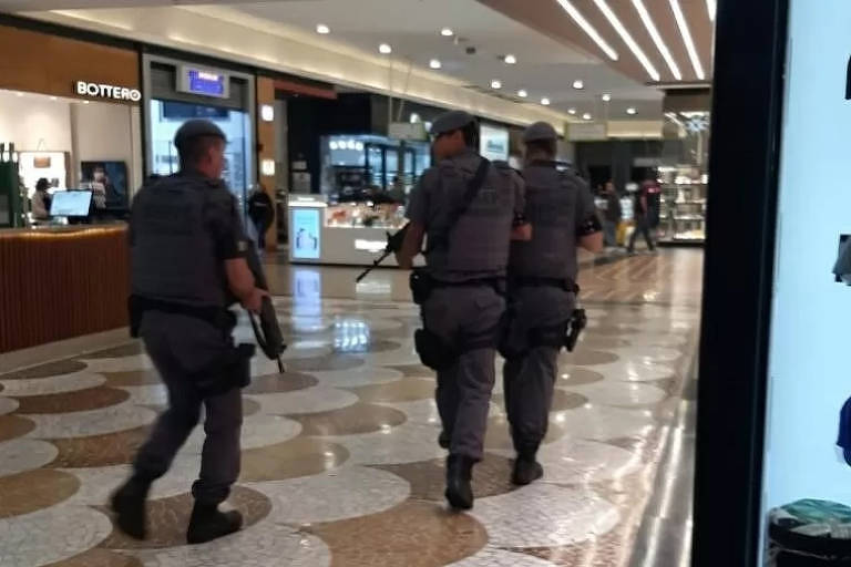 Imagem mostra três policiais de costas andando no corredor de um shopping