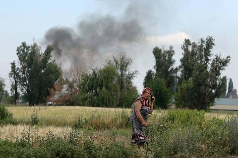 TOPSHOT - A woman speaks on a mobile phone on a roadside while smoke rises behind in the village Sviato-Pokrovske, Donetsk region, on June 23, 2022, amid Russia's military invasion launched on Ukraine. - On the road between the towns of Siversk and Bakhmut, AFP journalist witnessed several shellings on the route, which is now the main itinerary being used to reach the city of Lysychansk, since a highway has long been under shelling. Driving out of the devastated eastern Ukrainian city of Lysychansk on June 23, the journalists twice had to jump out of cars and lie on the ground as Russian forces shelled the city's main supply road. The three shelling incidents they witnessed took place on a stretch of road approximately 5 kilometres (3 miles) long. (Photo by Anatolii Stepanov / AFP)