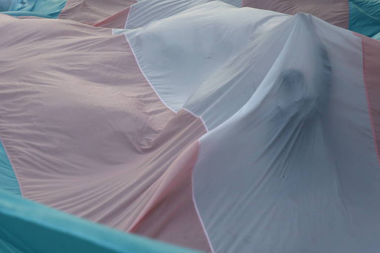 Pessoa debaixo de manta com as cores do orgulho trans (azul, rosa e branco)