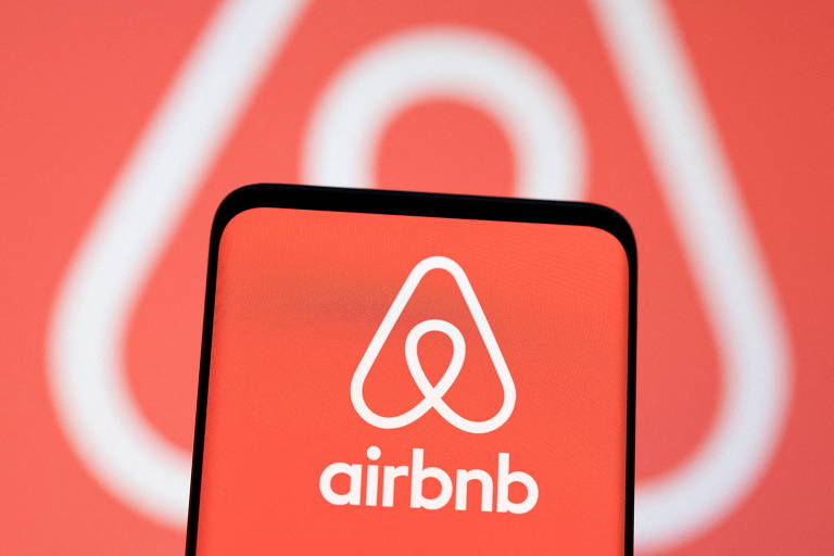Celular com logo do Airbnb. Ao fundo, logo do Airbnb desfocada.