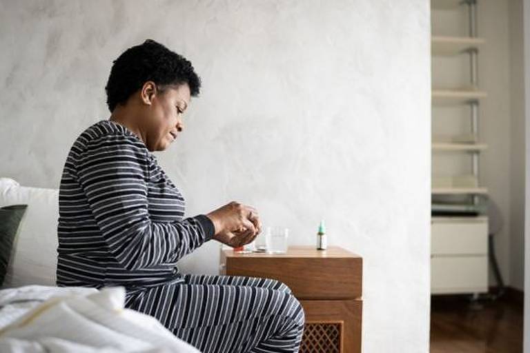 Imagem em primeiro plano mostra uma mulher negra de perfil sentada na beira de uma cama