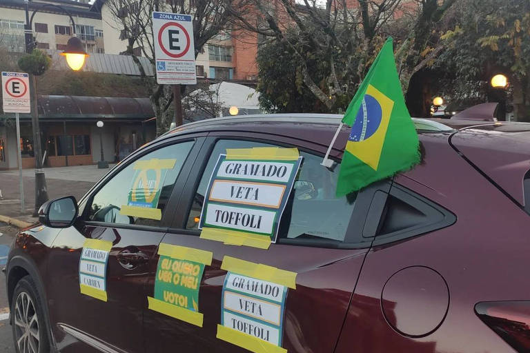 Carro bordô tem bandeiras do Brasil penduradas nos vidros e adesivos nas janelas com os dizeres Gramado Veta Toffoli e Gramado Veta Cármen.